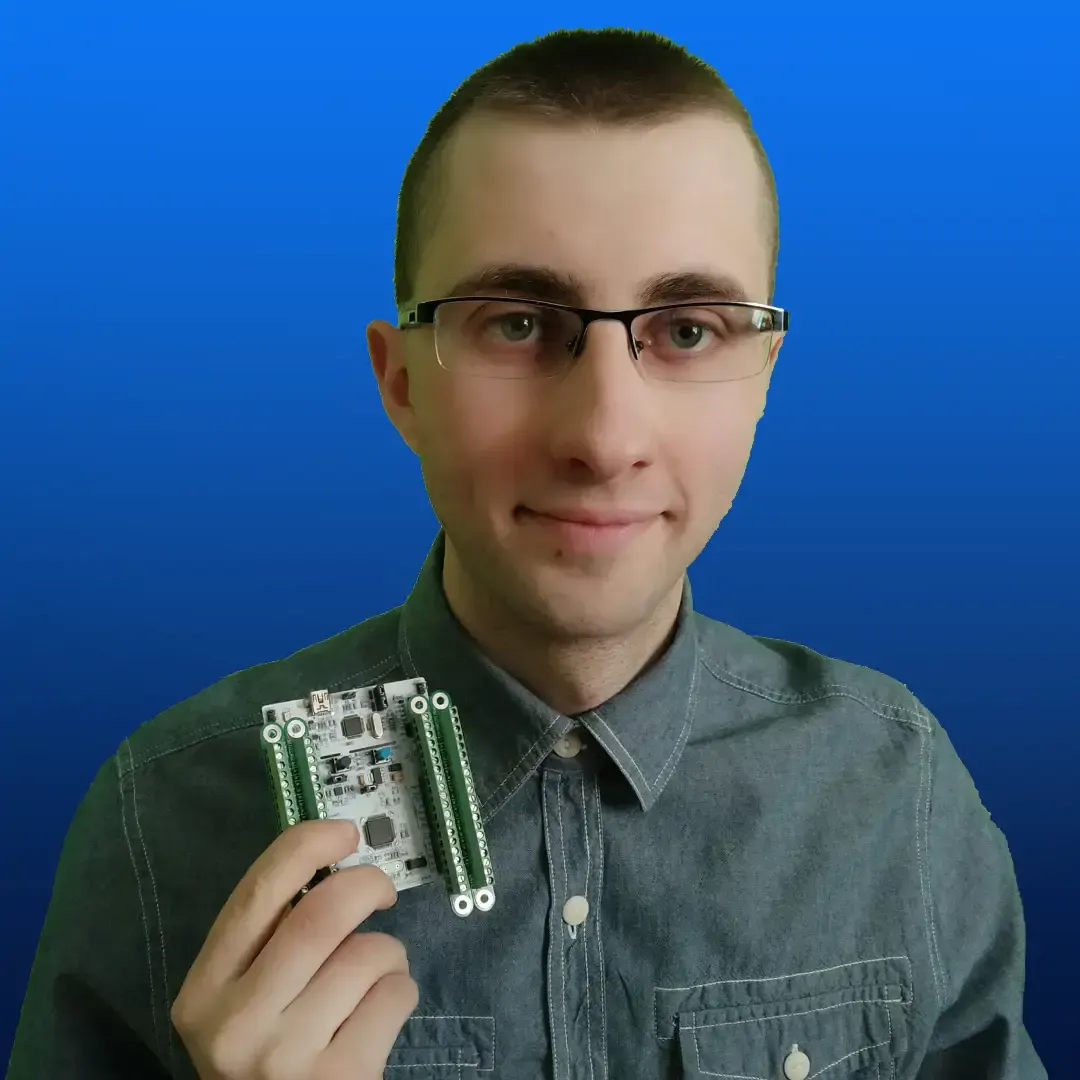 Łukasz Miłoś trzymający płytkę ewaluacyjną - znak, że znajmuje się także elektroniką i programowaniem embedded.